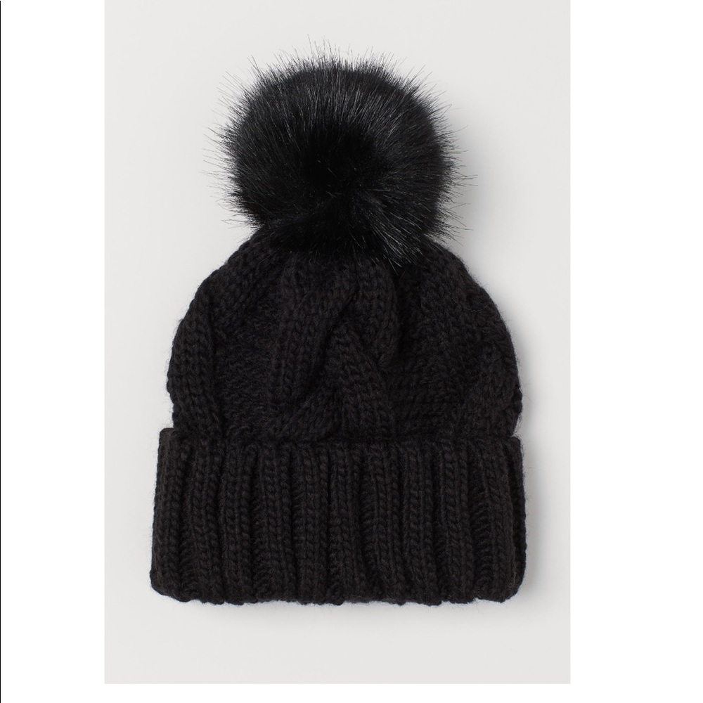 Soft cable knit hat with a faux fur pompom at top. Sewn, fold over cuff